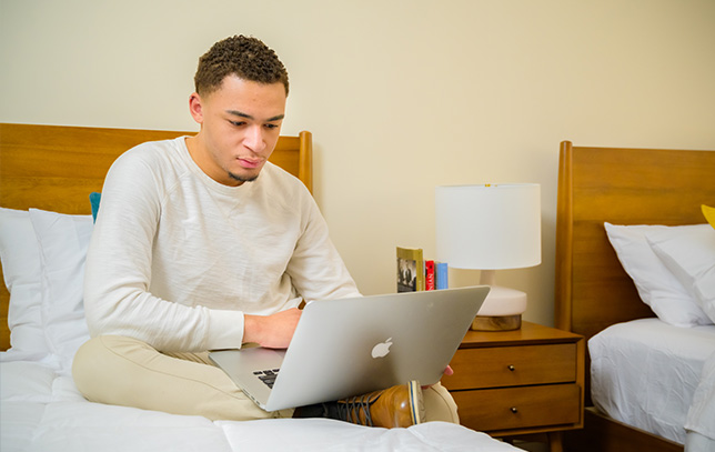 a patient on his laptop while sitting on his bed